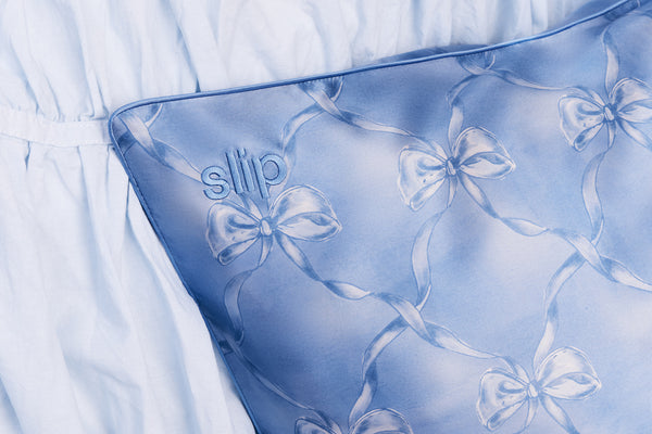 Blue silk pillowcase with bow pattern and 'slip' embroidery on a light blue background