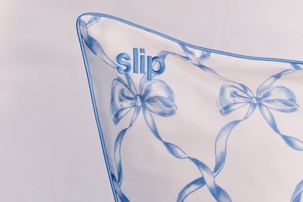 Pillow with blue ribbons and 'slip' embroidery on a light gray background