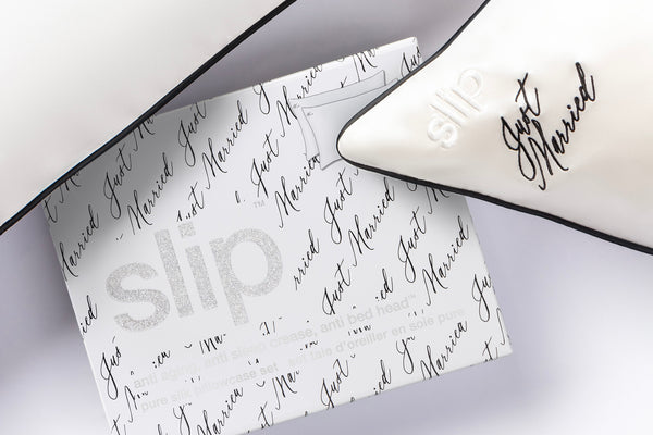 Close up of 'just married' embroidery in black on a white silk pillowcase and silver glitter slip logo on packaging.