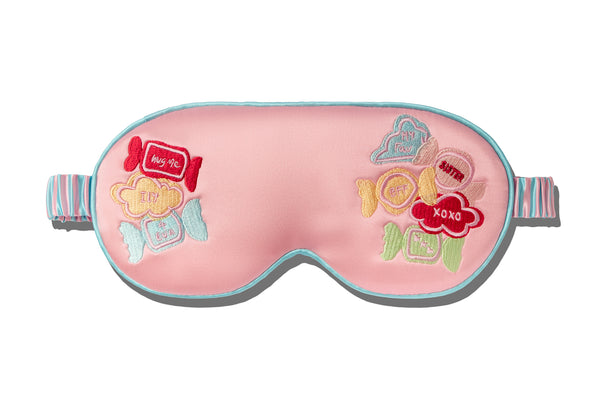 Pink sleep mask with colorful designs and text on a white background