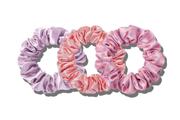 A set of three large slip silk scrunchies in shades of purple, pink, and rose on white background.