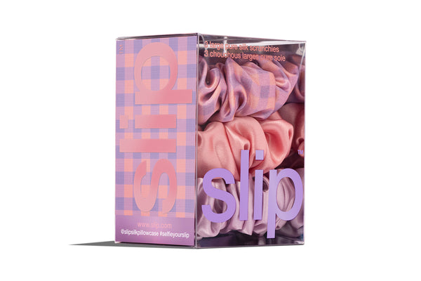 A set of three large slip silk scrunchies in shades of purple, pink, and rose in branded packaging on white background.