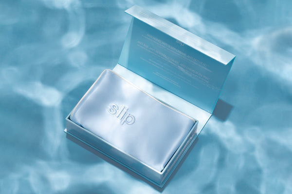 A seabreeze blue slip queen pillowcase with an invisible zipper closure. Displayed in open branded packaging on a blue water background.