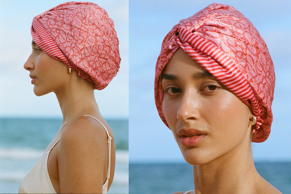 A model wearing a red and pink striped slip silk turban with twist detail.