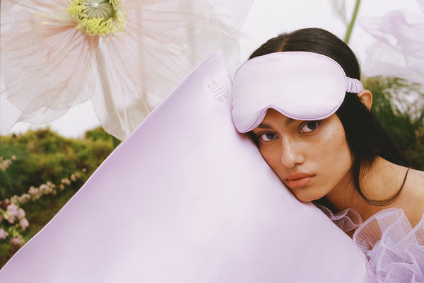 Woman holding a lilac slip silk queen pillowcase, wearing a slip lilac contour mask.