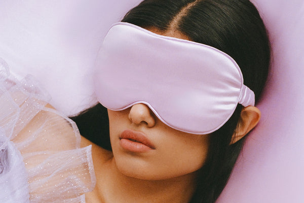 A woman wearing a purple slip silk contour sleep mask, designed for eyelash extension wearers.