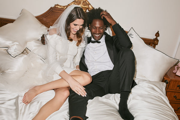 A bride and groom lounging on white slip pure silk pillowcases with black piping.