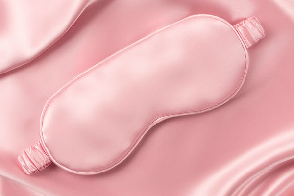 A pink slip silk sleep mask on a pink silk background.