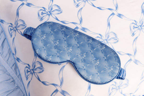 Blue contour sleep mask with bow pattern on a white pillow with blue bow design