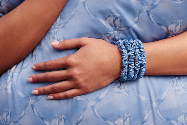 Hand wearing a blue scrunchie on a blue bow fabric background