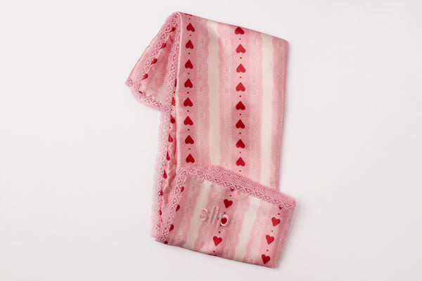 Folded pink pillowcase with heart patterns on a light gray background